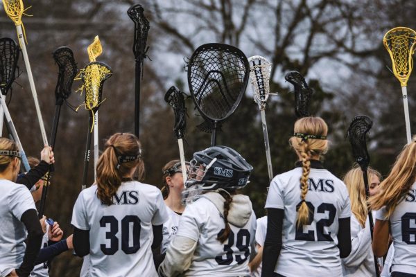 Varsity lacrosse players raise their sticks in the air before taking the field.